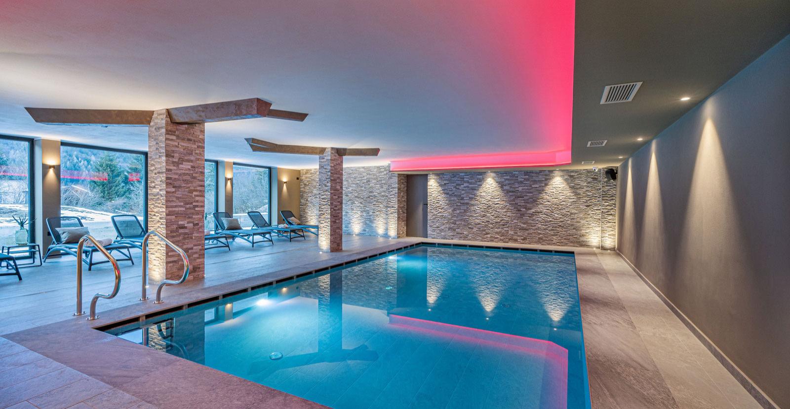 Modern indoor pool with loungers and soft lighting in a relaxing environment.