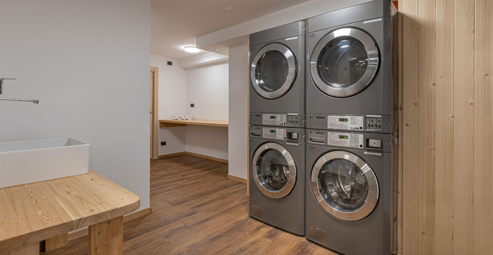 Modern laundry room with stacked washers and wooden flooring.