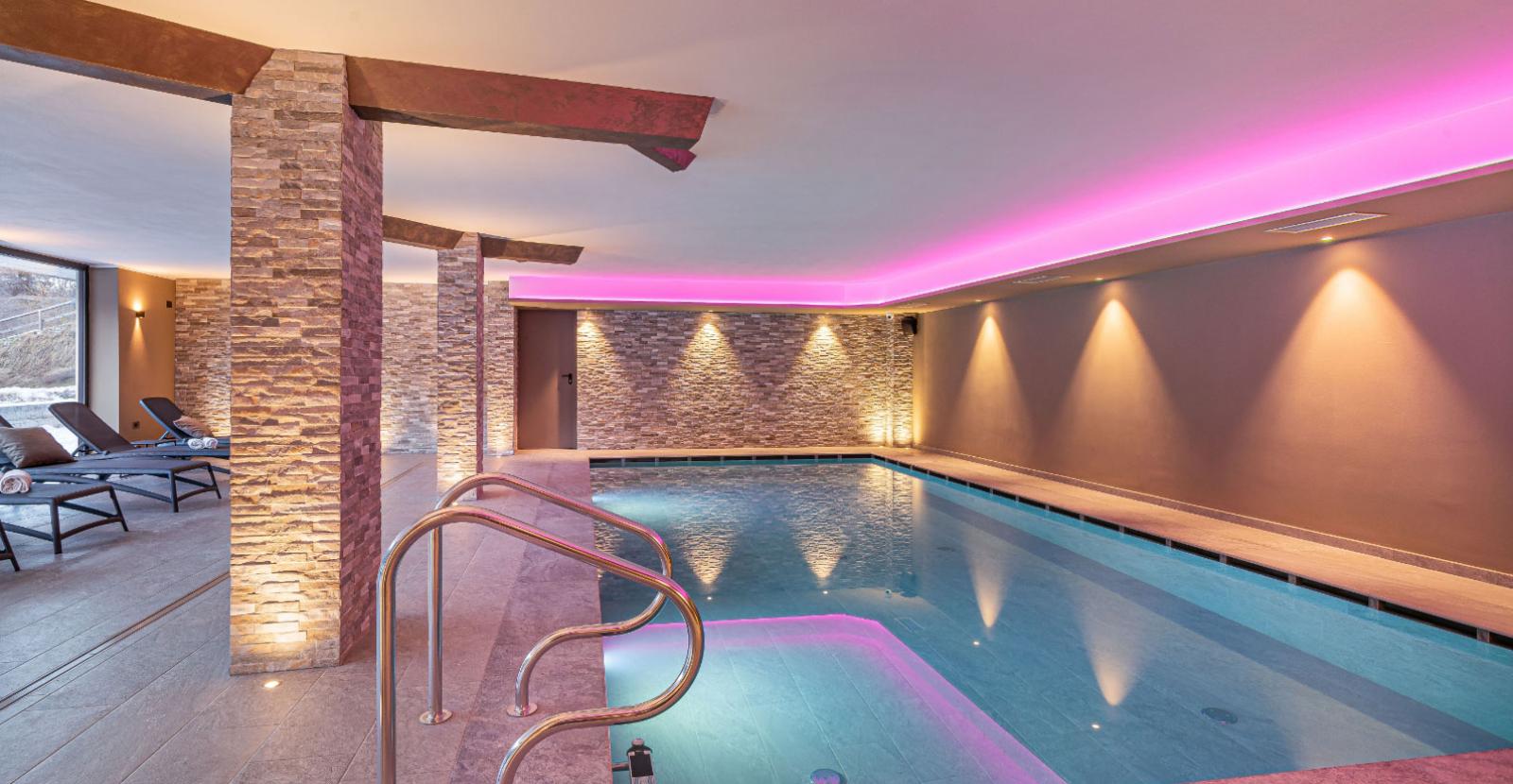 Indoor pool with pink lighting and relaxation loungers.
