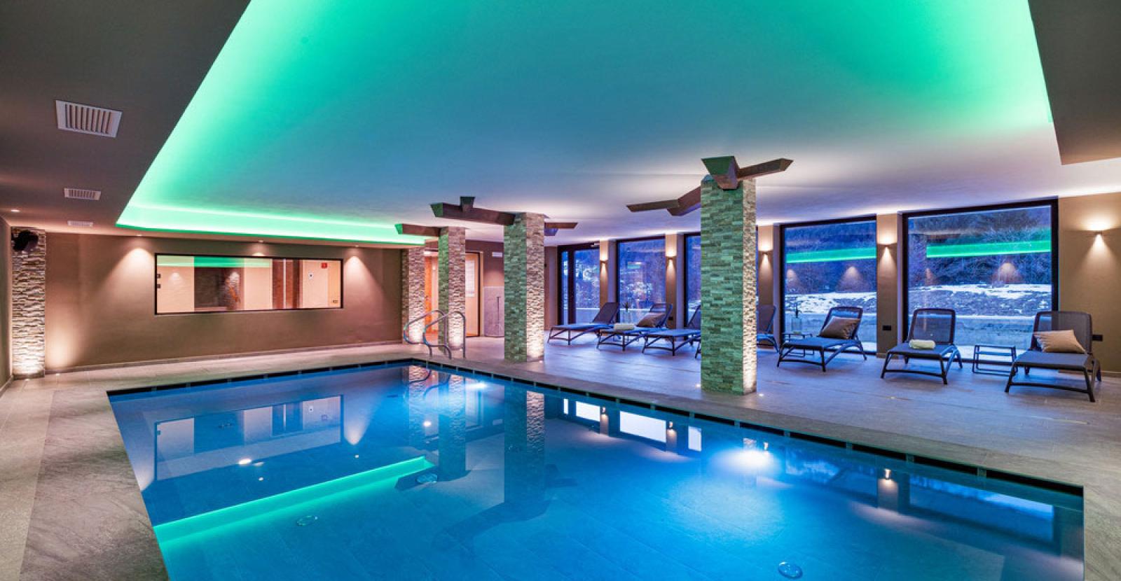 Modern indoor pool with soft lighting and lounge chairs for relaxation.