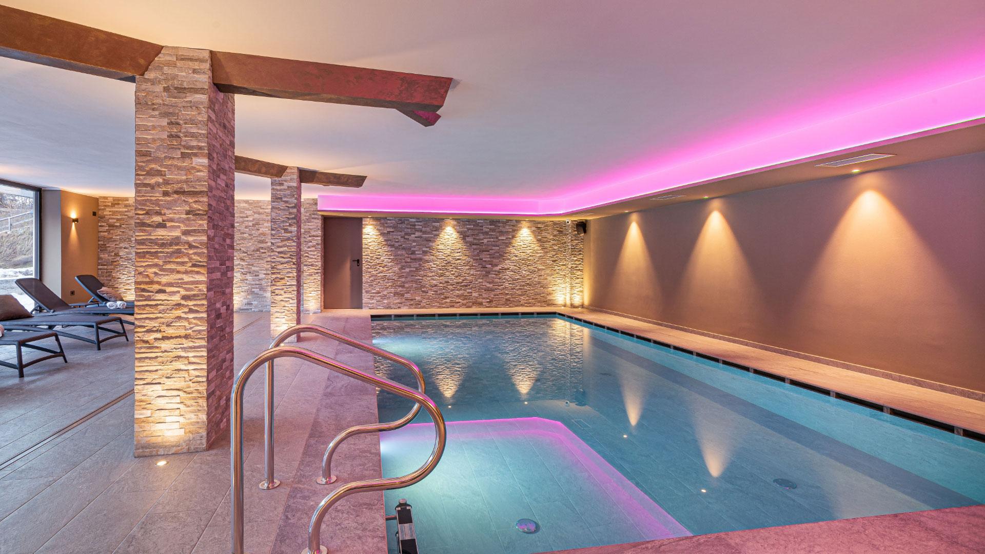 Indoor pool with soft lighting and lounge chairs for relaxation.