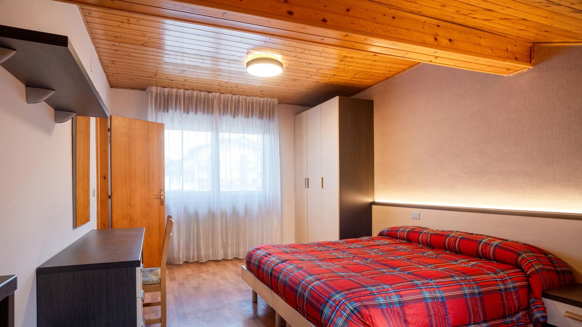 Cozy bedroom with wooden ceiling and bed with red checkered blanket.