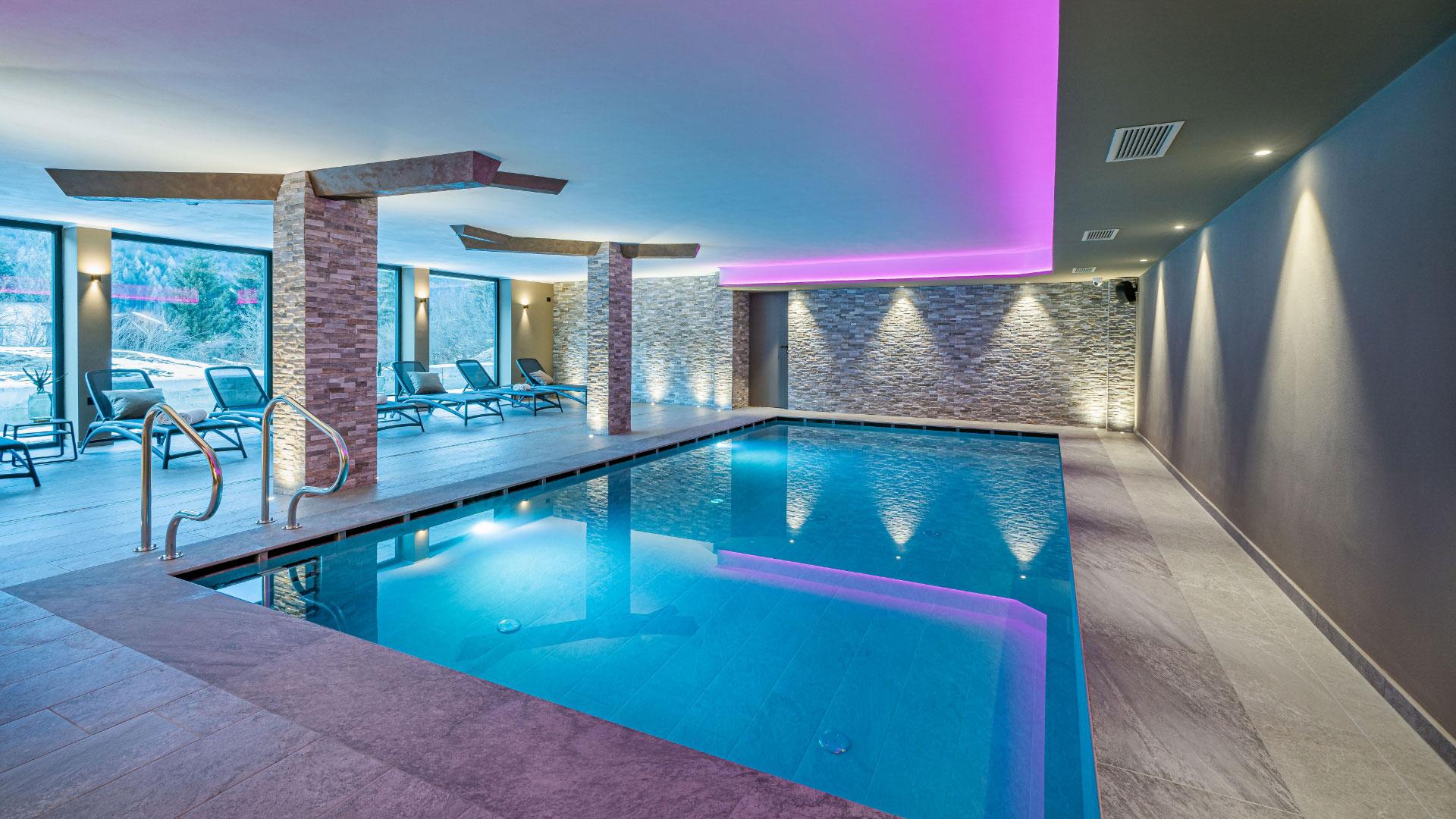 Indoor pool with soft lighting and relaxation loungers.