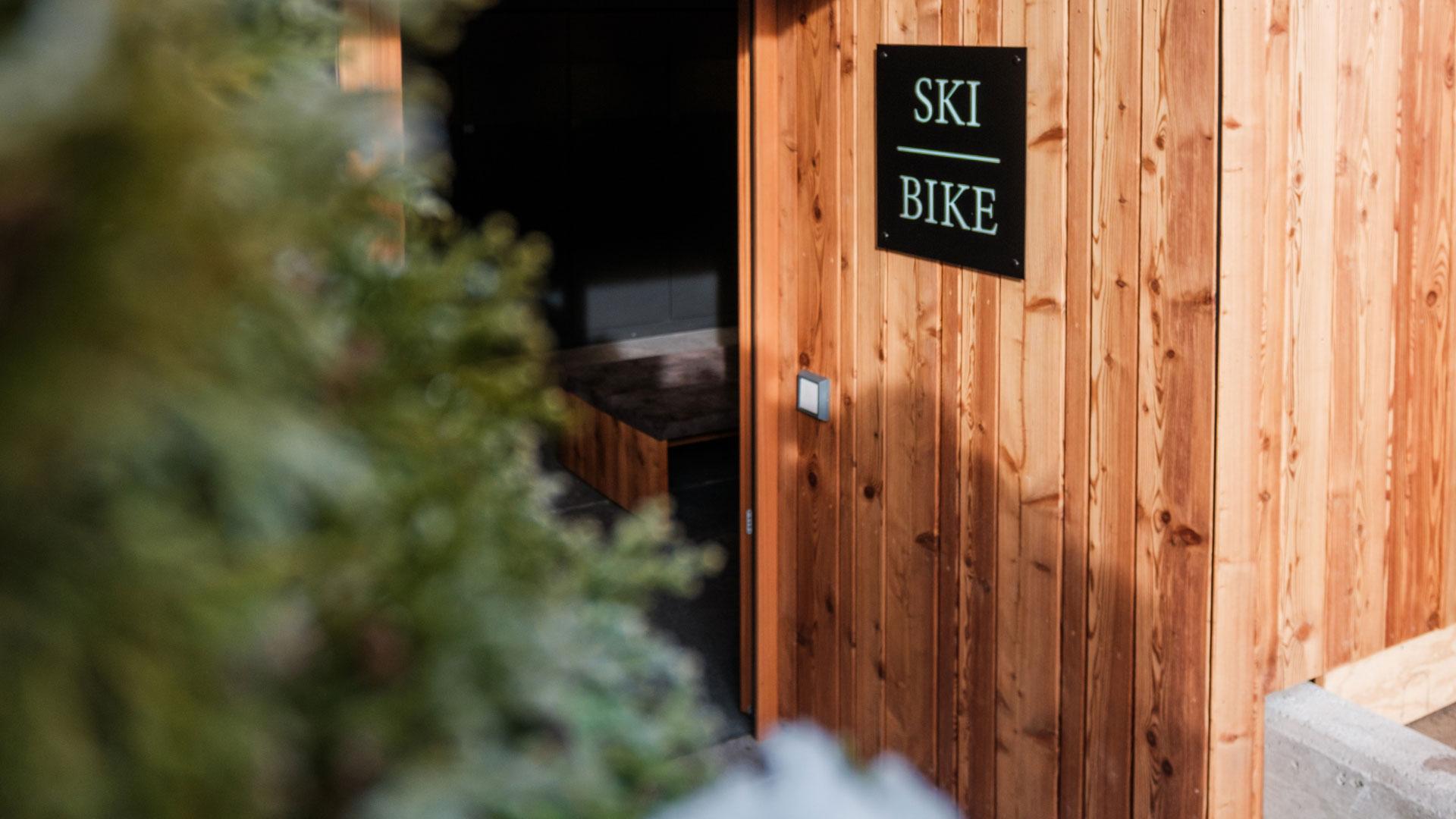 Wooden entrance with ski and bike sign, green background.