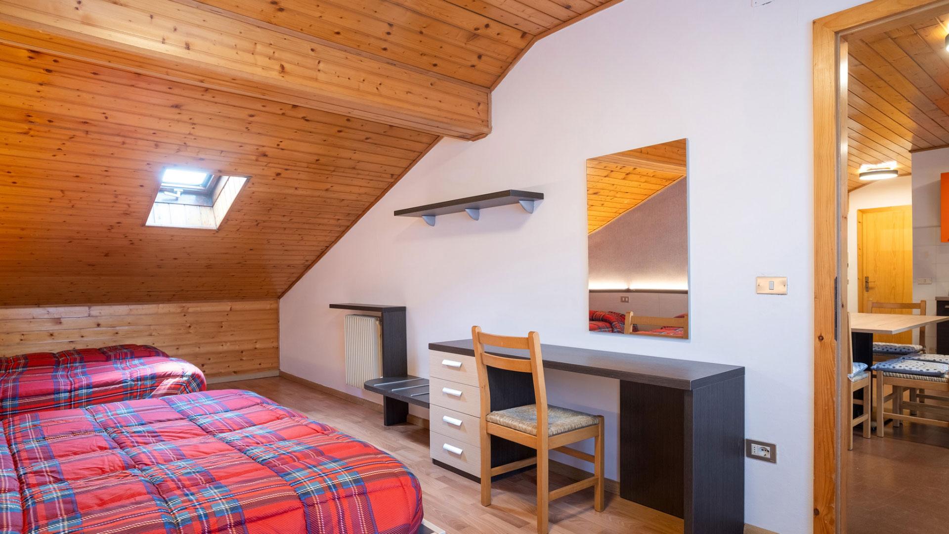 Attic room with two beds and desk, wooden ceiling.