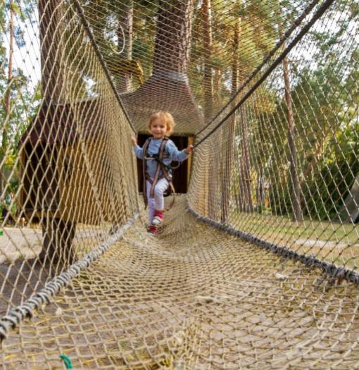Bambina attraversa ponte di rete in un parco avventura tra gli alberi.