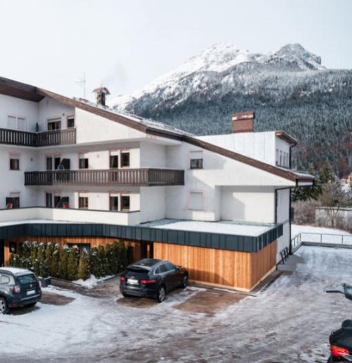 Snowy alpine building with parking, mountains in the background.