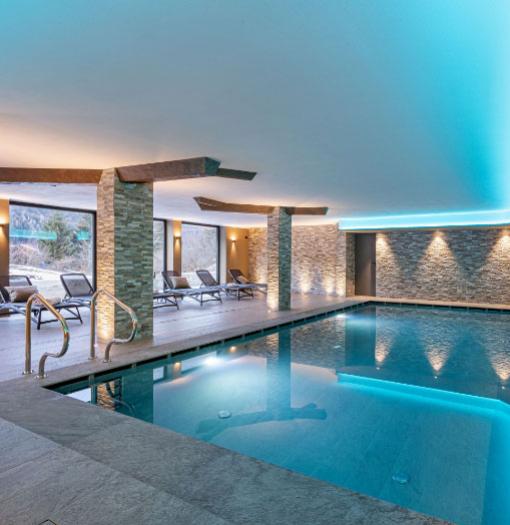 Modern indoor pool with loungers and soft lighting.