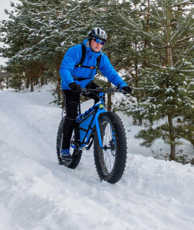 Cyclist on a blue fat bike rides a snowy trail among trees.