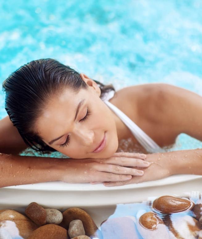 Donna rilassata in piscina con pietre decorative, occhi chiusi.