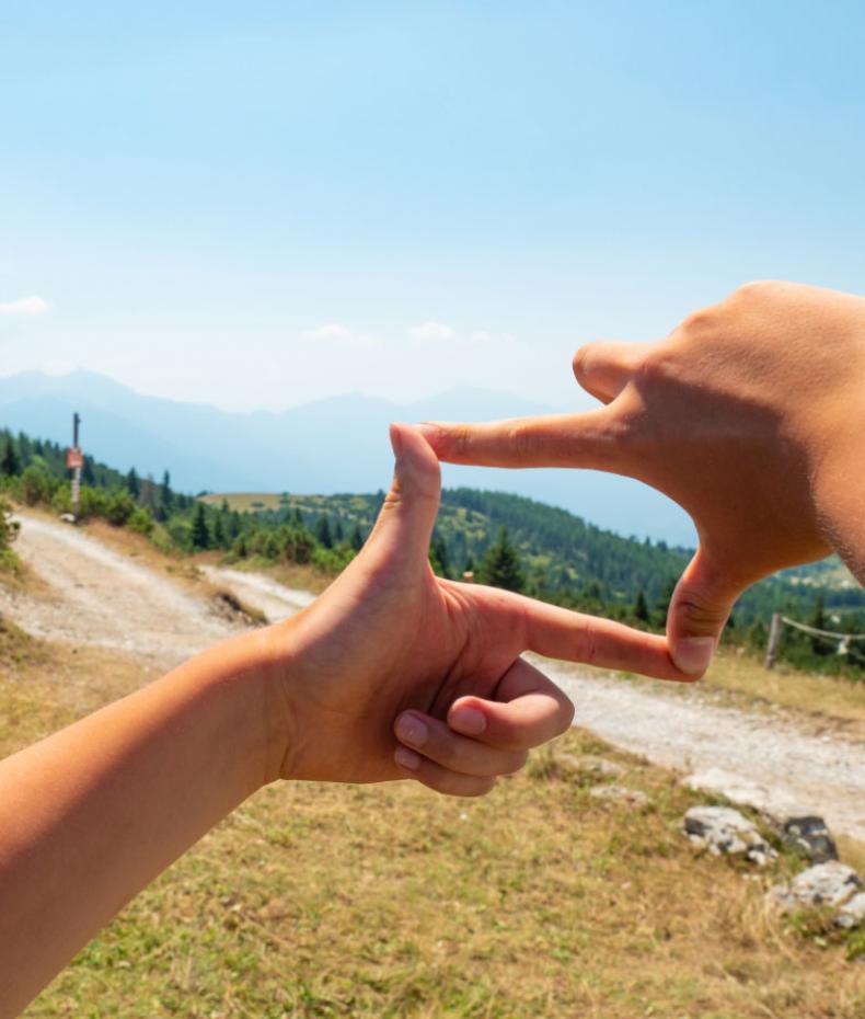 Hands forming a rectangle with a mountain landscape in the background.