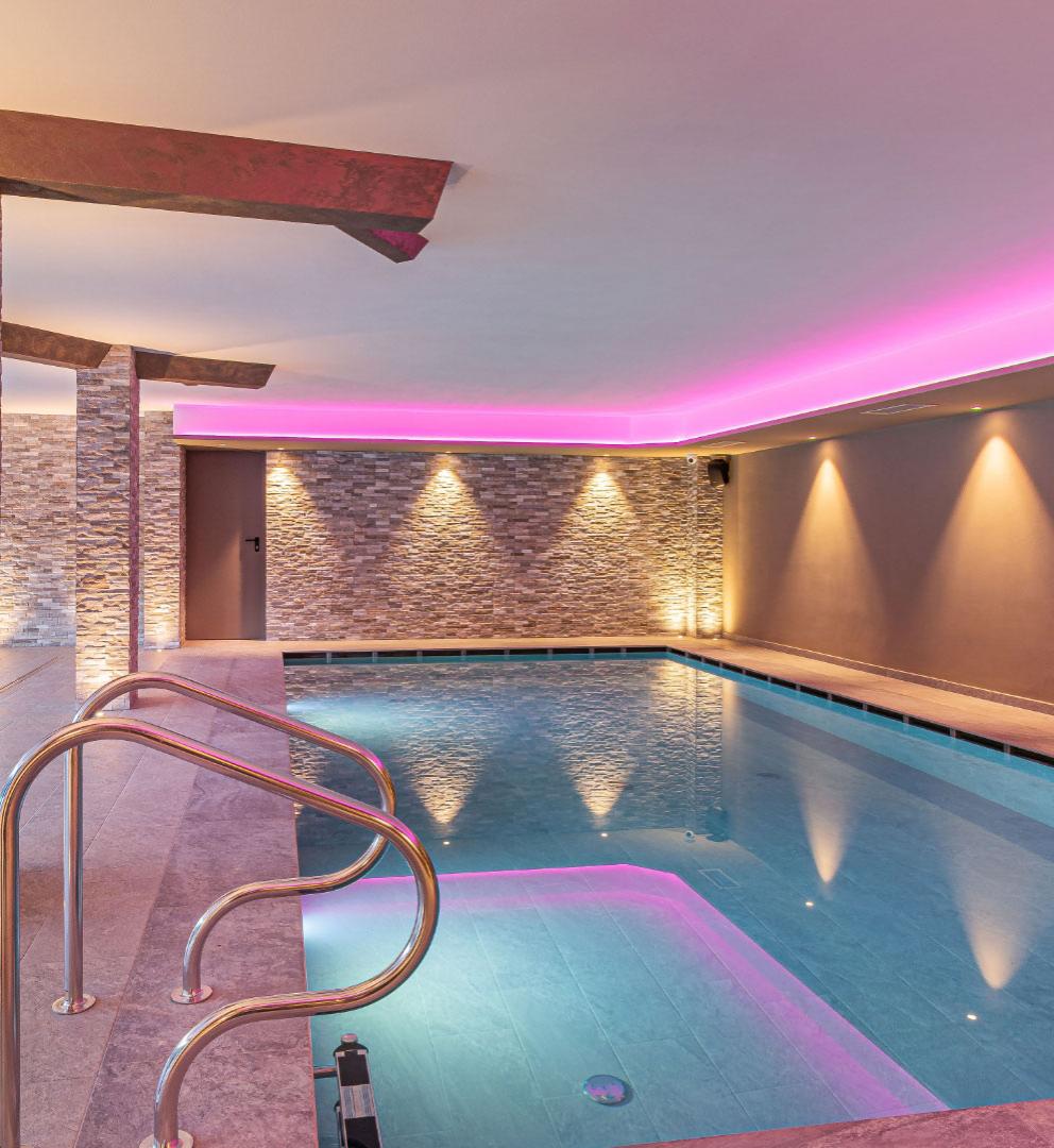 Indoor pool with soft lighting and lounge chairs for relaxation.