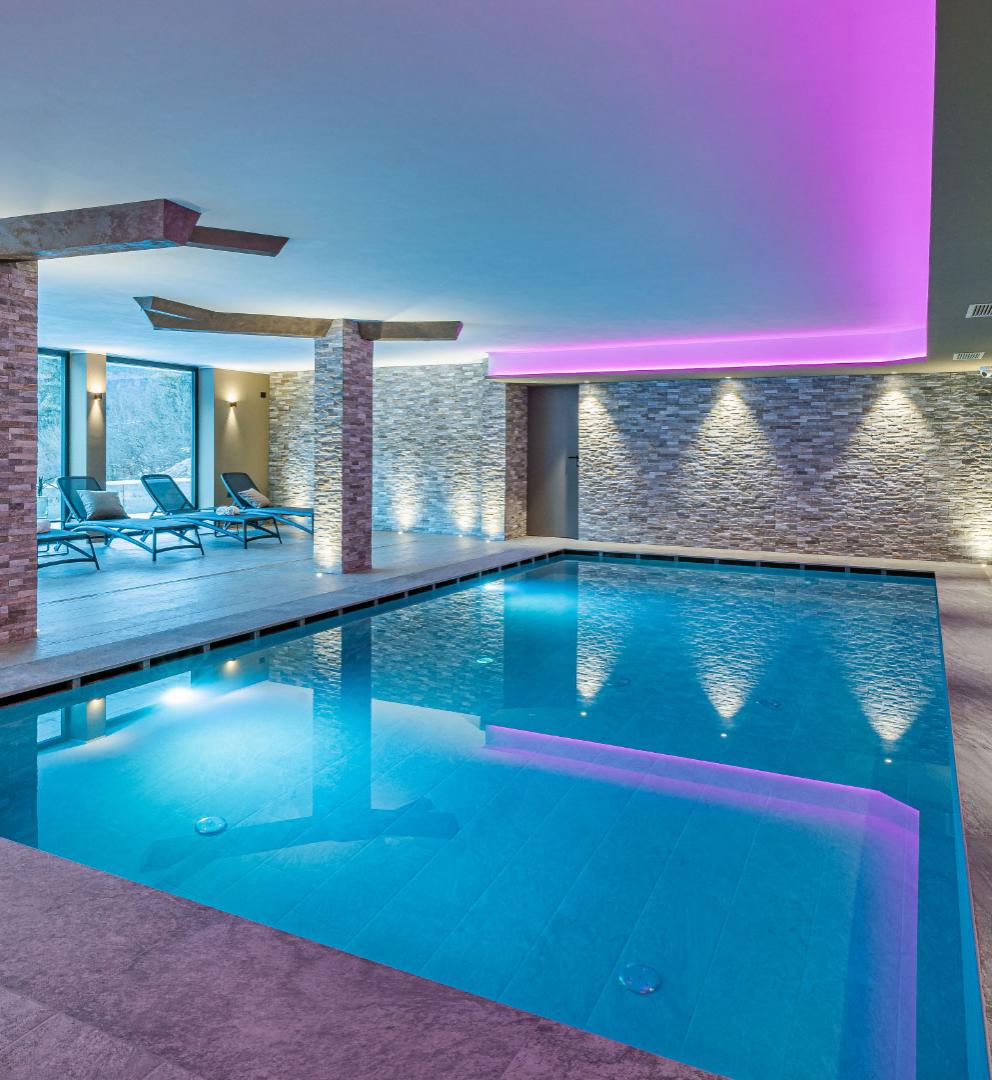 Indoor pool with soft lighting and relaxation loungers.